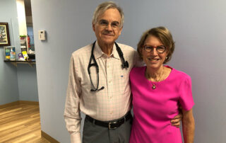 William-Kelly,-MD,-and-wife,-Joanelle-Kelly,-posing-for-a-picture-from-their-Kernersville-Primary-Care-clinic-in-Kernersville,-NC.